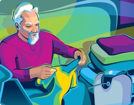 An older man receiving oxygen supplementation from an oxygen concentrator while sitting on his couch and folding his laundry.