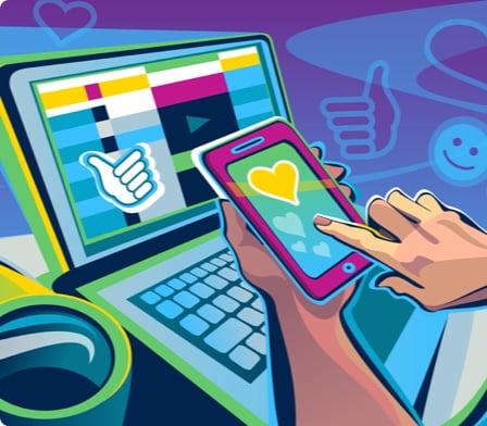 Hands using a smartphone in front of an open laptop computer.